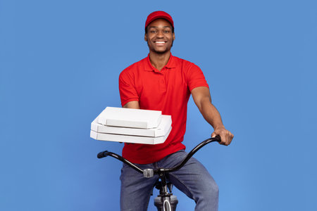 Black delivery man holding pizza boxes, riding bicycleの写真素材