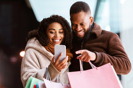Smiling black couple using smartphone with shopping bagsの写真素材