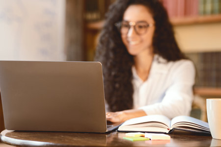 Woman sitting at desk, using laptop, focus on notebook