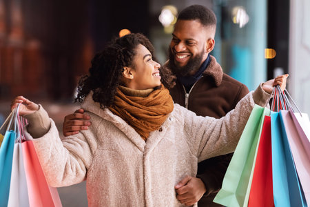 Happy afro couple hugging and holding colorful shopping bagsの写真素材
