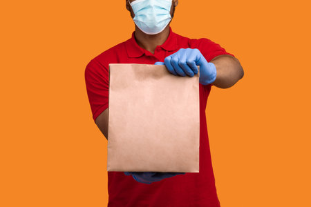 Black delivery man in medical mask and gloves holding packageの写真素材