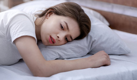 Young woman lying alone in her bed, mourning about loss of loved one, suffering from severe depressionの写真素材
