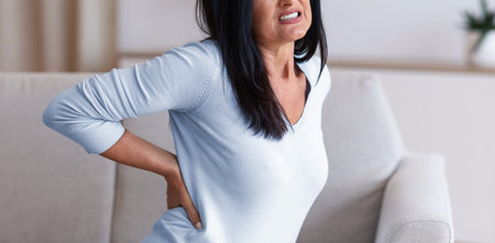 Mature woman having back pain while sitting on couch
