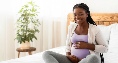Maternity Concept. Happy Expectant Black Lady Posing On Bed At Home
