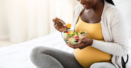 Black Pregnant Woman Holding Bowl With Fresh Vegetable Salad, Enjoying Healthy Nutritionの写真素材