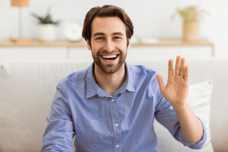 Happy Man Waving Hand To Camera Sitting At Homeの写真素材