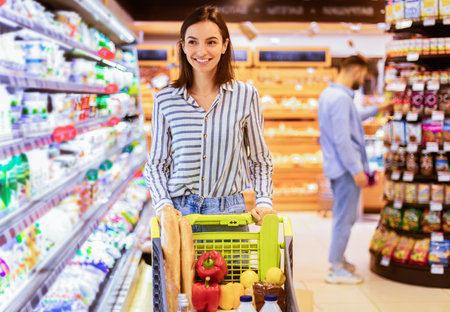 Young smiling woman shopping in supermarket with trolley cartの写真素材