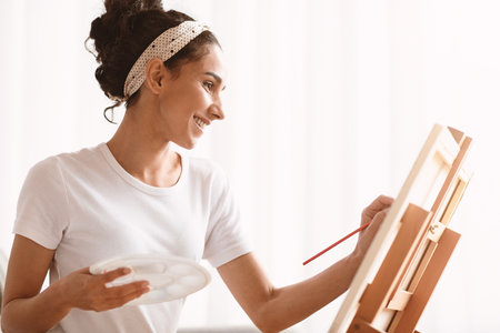 Young woman artist painting at home, side viewの写真素材