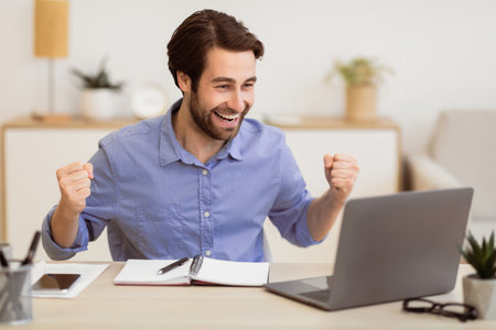Guy At Laptop Celebrating Success In Modern Officeの写真素材