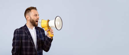 Confident millennial man in formal wear shouting into megaphone on grey studio backgroundの写真素材