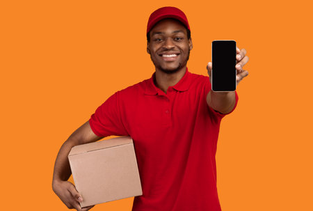 Black courier showing cellphone with blank screen, holding boxの写真素材