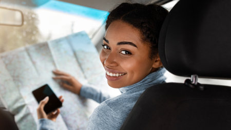 Smiling attractive cute young african american woman driver researching map and holding phoneの写真素材
