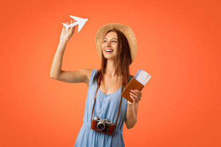 Cheerful pretty girl with camera holding passport and paper airplane