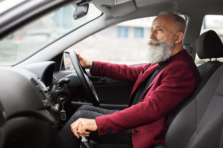 Bearded aged businessman driving luxury car, shot inside vehicle