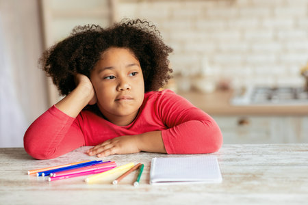 Boredom. Cute little bored black girl sitting at table in kitchen