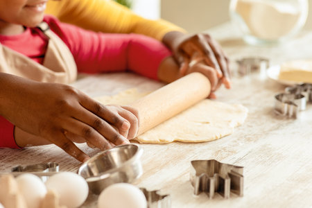 Black mom and daughter rolling up dough for cookies in kitchen togetherの写真素材