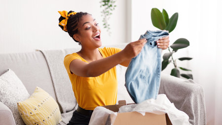Happy black woman unpacking clothes after online shopping
