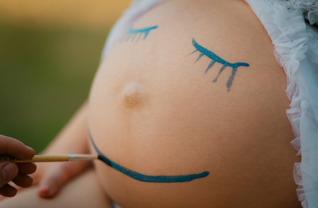 Pregnant woman belly closeup with smiling funny face drawingの写真素材
