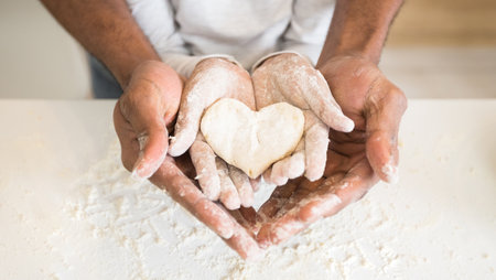 Afro man hands holding child hands with heart shaped pastryの写真素材