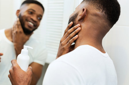 Young black man applying moisturizer on beard in bathroomの写真素材