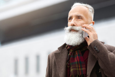 Elderly businessman walking by city, having phone callの写真素材