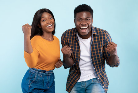 Portrait of excited young black couple shaking clenched fists