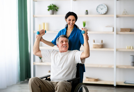 Post-stroke rehabilitation. Female physiotherapist helping elderly male patient in wheelchair to...