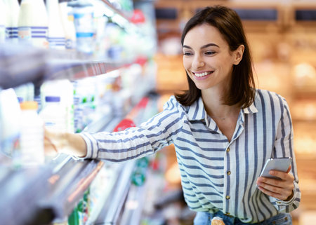 Woman holding smartphone standing in store taking milkの写真素材