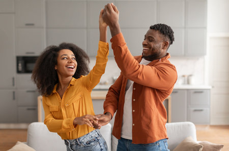 Cheerful millennial black spouses having fun together dancing in kitchenの写真素材