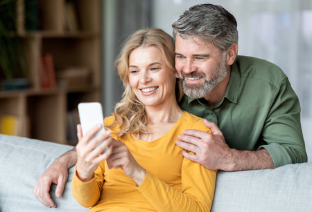 Portrait Of Smiling Middle Aged Couple Resting With Smartphone On Couchの写真素材