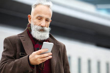 Grey-haired businessman using smartphone on the streetの写真素材