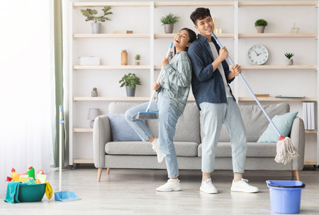 Happy asian couple singing songs while cleaning apartment, copy spaceの写真素材