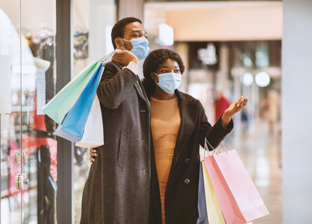 Happy african american family in coats and protective masks walking in mall after buying clothes at Black Fridayの写真素材