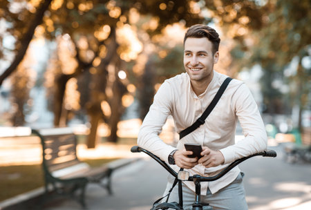 Street style. Young stylish man texting on phone while sitting on bikeの写真素材