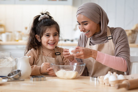 Happy islamic mom and her cute daughter preparing dough in kitchen togetherの写真素材