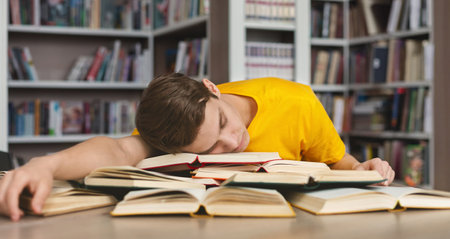 Tired guy napping on books in libraryの写真素材