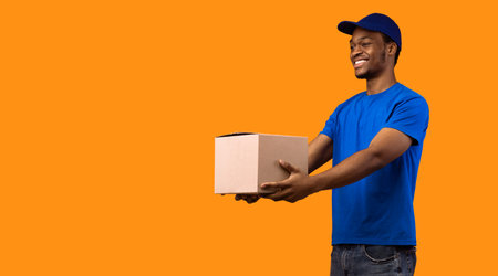 Black delivery man holding cardboard box giving it to sideの写真素材