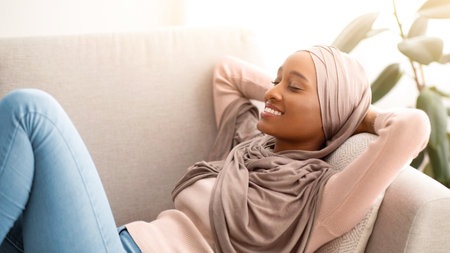 Lovely black lady in hijab lying on sofa, closing her eyes and smiling, taking nap at midday,...