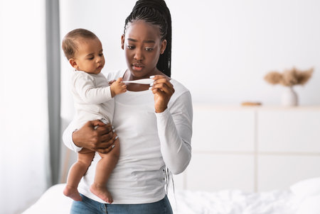 Scared young African American mother looking at thermometerの写真素材