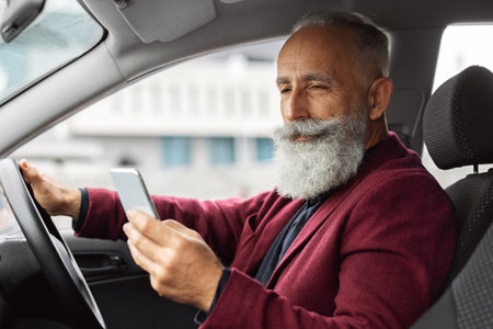 Elderly man driving new car, using mobile phone