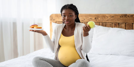 Pregnant black woman choosing between healthy and unhealthy food at homeの写真素材
