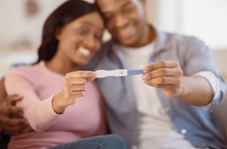 Young balck couple showing positive pregnancy test at home, selective focus on handsの写真素材