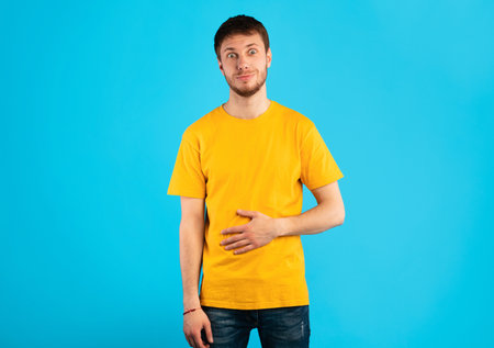 Young satisfied man touching his stomach at studioの写真素材