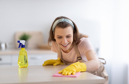 Cheerful young housewife washing table with rag and detergent at kitchen, panorama. Sanitary service conceptの写真素材