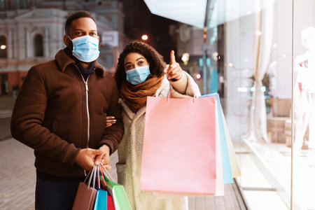 Excited black woman in mask showing her husband mall windowの写真素材