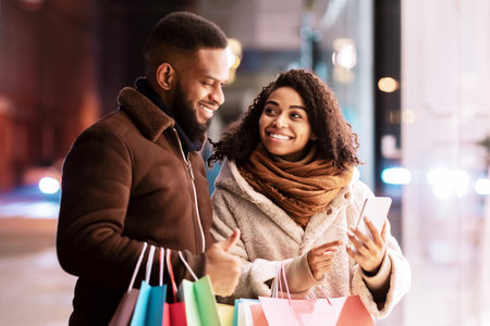Happy afro couple using smartphone with shopping bagsの写真素材