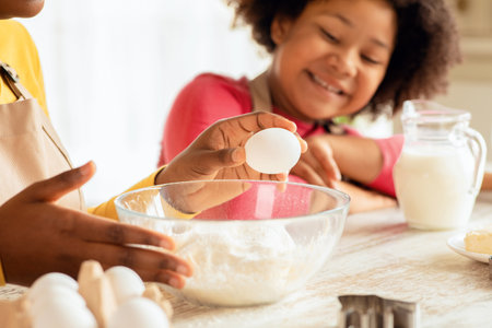 Black mother and little daughter preparing dough for cookies in kitchen togetherの写真素材