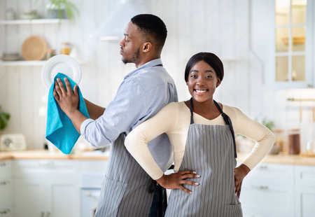 Portrait of positive black woman and her husband wiping dishes at kitchenの写真素材