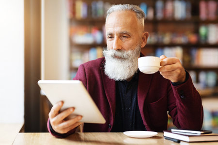 Wealthy grey-haired elderly man drinking coffee and using digital tablet