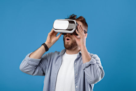 Cool millennial guy experiencing virtual reality in VR headset on blue studio background